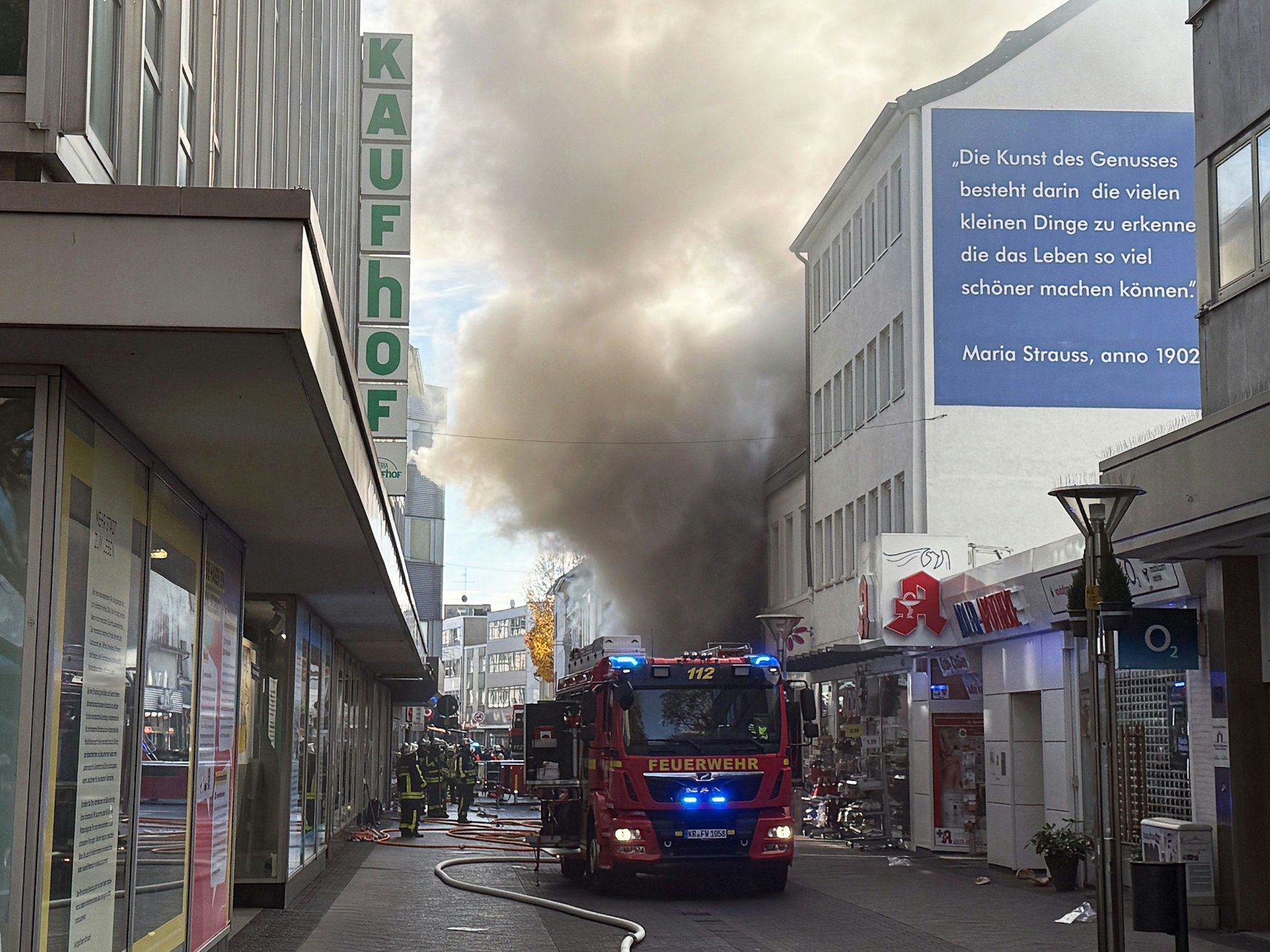 Einsatzkräfte stehen in einer Einkaufstraße vor einem Geschäft, aus dem dichter Rauch quillt. Ein Feuer in einem Laden der Einkaufsmeile Hochstraße hat einen Großeinsatz der Feuerwehr in der Innenstadt ausgelöst.