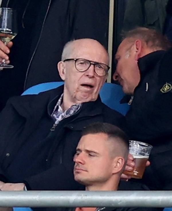 Reiner Calmund sitzt auf der Tribüne und bekommt von seinem Sitznachbarn etwas ins Ohr gesagt.