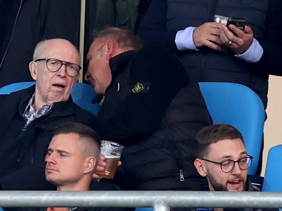 Reiner Calmund sitzt auf der Tribüne und bekommt von seinem Sitznachbarn etwas ins Ohr gesagt.