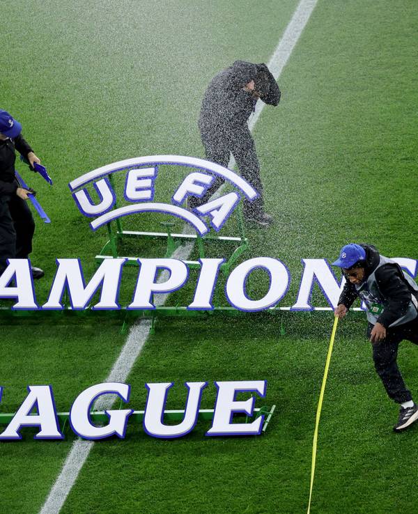 Der Champions League Schriftzug liegt auf dem Rasen, drei Mitarbeiter flüchten vor einem Wasserstrahl.