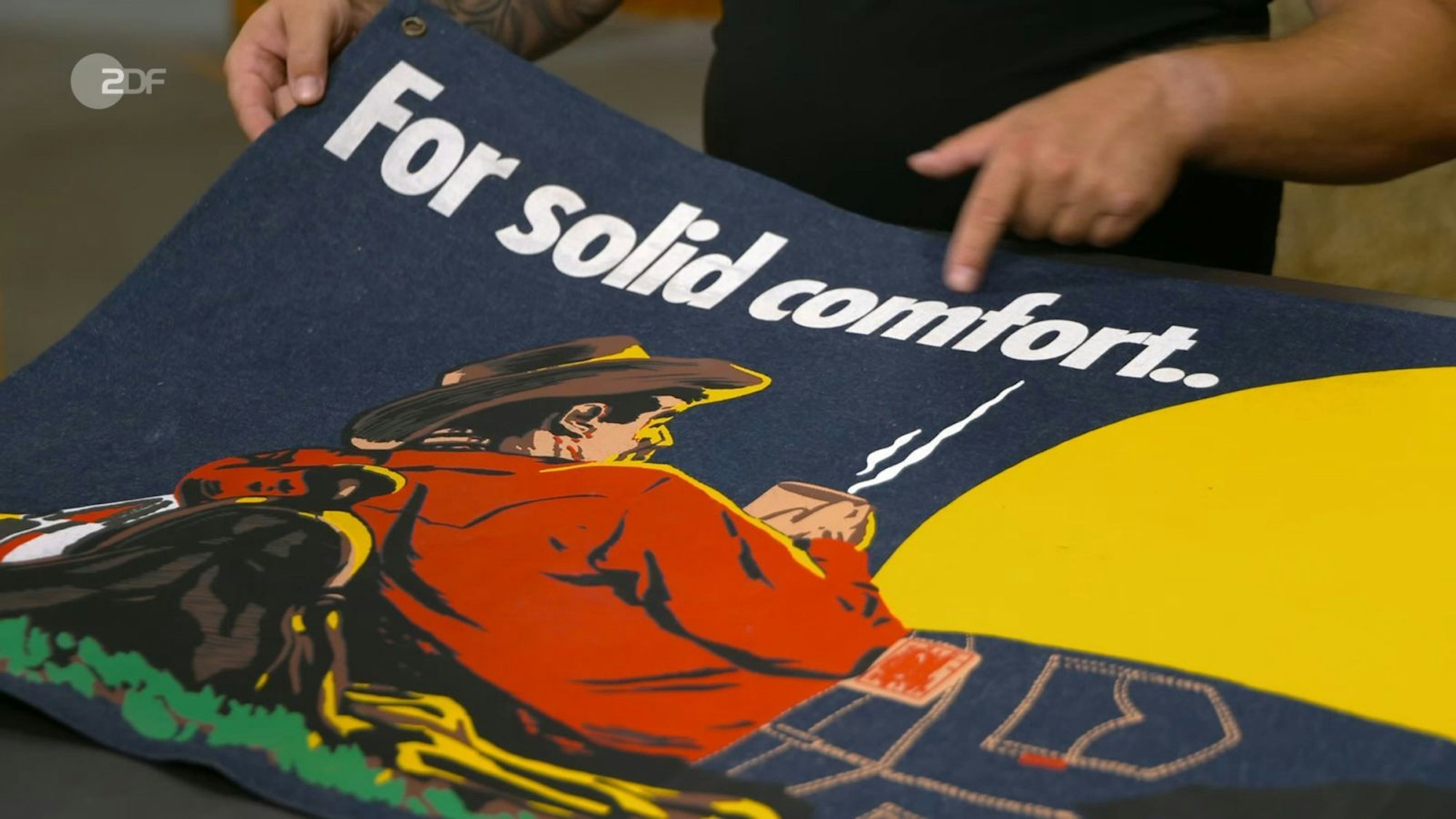 „For solid comfort“ und „America´s finest overall since 1850“ war darauf zu lesen. Das Motiv: ein Cowboy, der sich an seinen Sattel anlehnt, Kaffee trinkt und in den Sonnenuntergang schaut. (Bild: ZDF)
