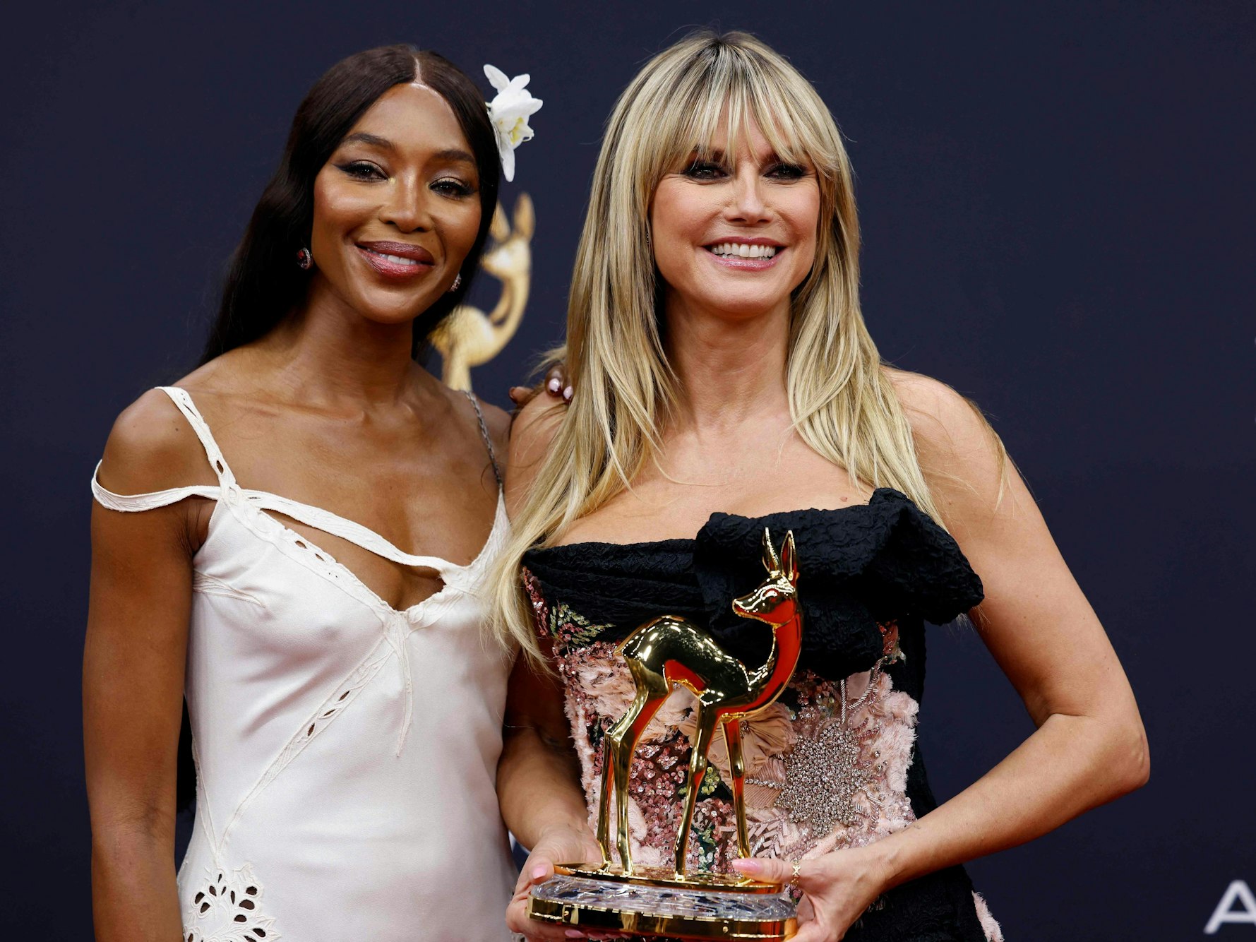 Zwei Frauen in schulterfreien Kleidern stehen nebeneinander, die ein hält eine Auszeichnung in Form eines Rehs in der Hand.