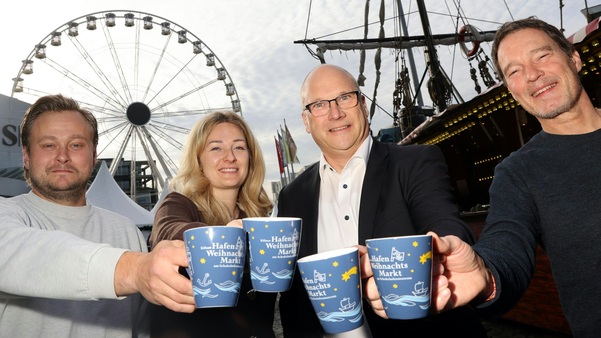 Vier Personen des Hafen-Weihnachtsmarktes stehen zusammen und stoßen mit Tassen an.