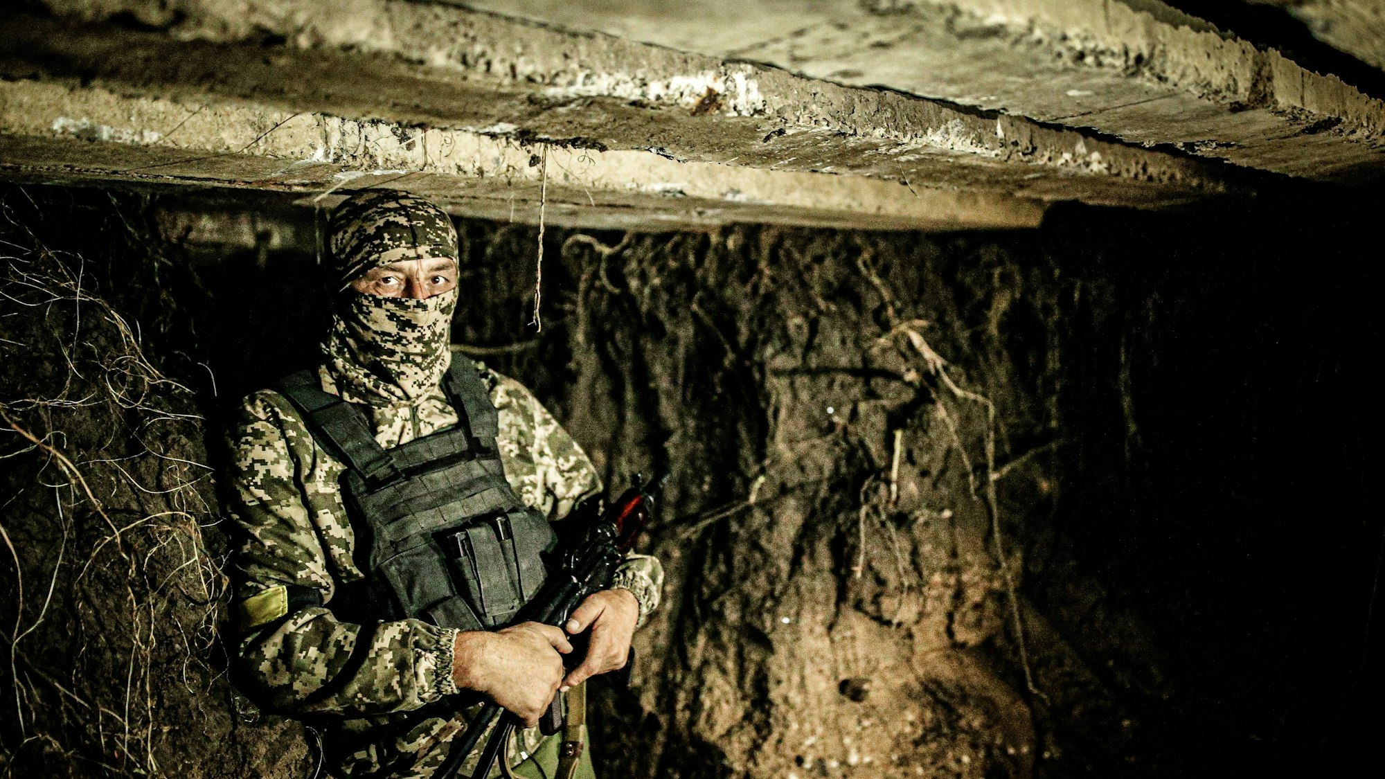 Soldat in Tarnuniform mit verdecktem Gesicht und Gewehr in einem dunklen Bunker