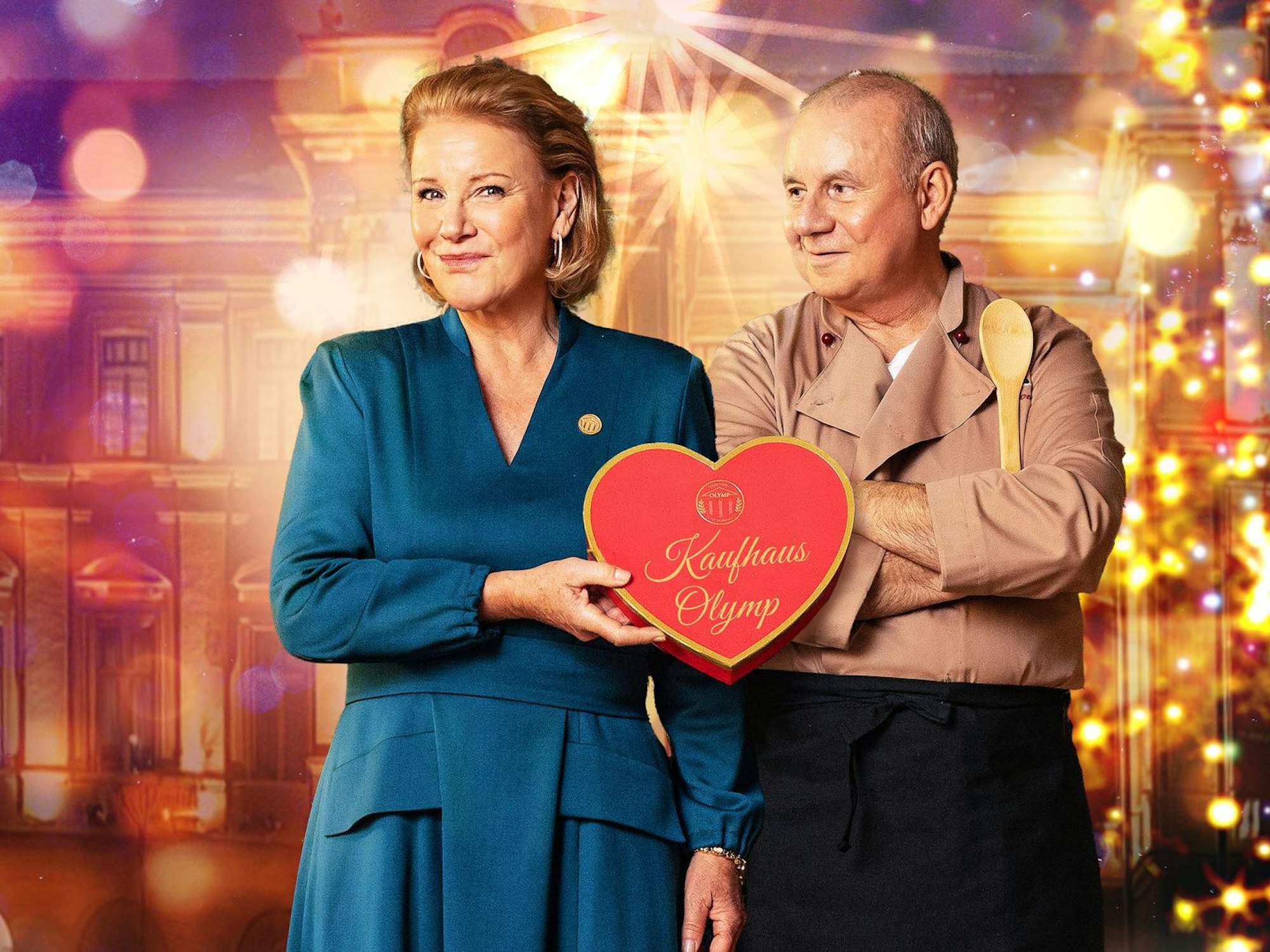Ein Mann und eine Frau stehen in Festtagskleidung vor einer strahlenden, goldenen Kulisse und halten ein Herz, auf dem "Kaufhaus Olymp" steht.