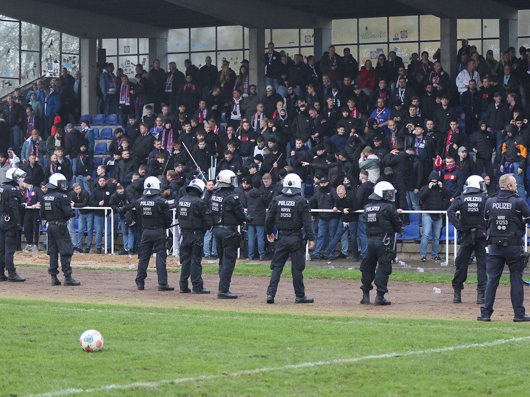 Einsatzkräfte stehen vor einer Fan-Tribüne, auf der es Ausschreitungen gibt.