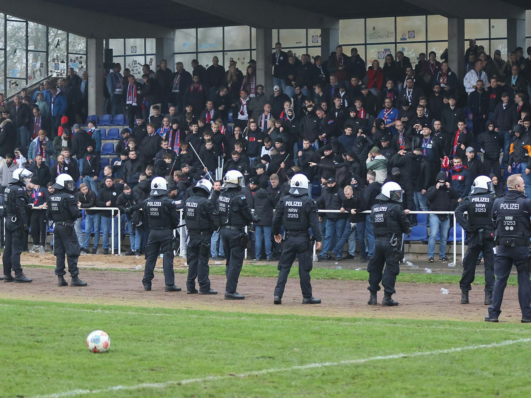 Einsatzkräfte stehen vor einer Fan-Tribüne, auf der es Ausschreitungen gibt.