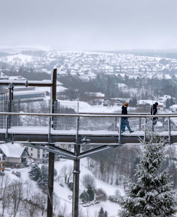 Spaziergänger gingen im Januar 2025 über den Skywalk neben der Bobbahn in Winterberg mit Blick auf die Landschaft im Schnee.