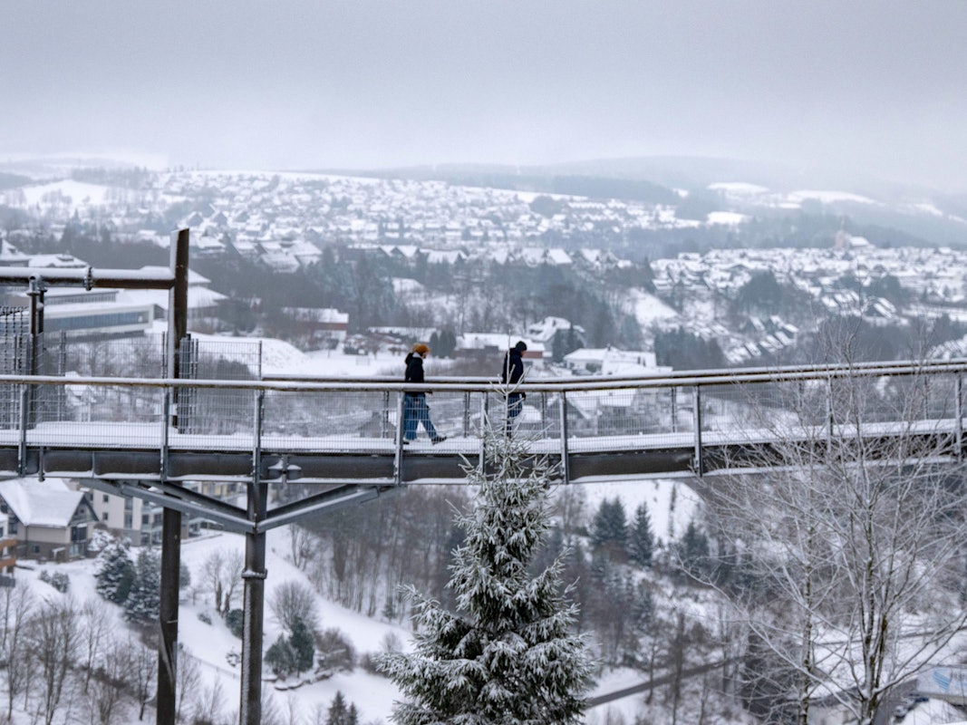 Spaziergänger gingen im Januar 2025 über den Skywalk neben der Bobbahn in Winterberg mit Blick auf die Landschaft im Schnee.