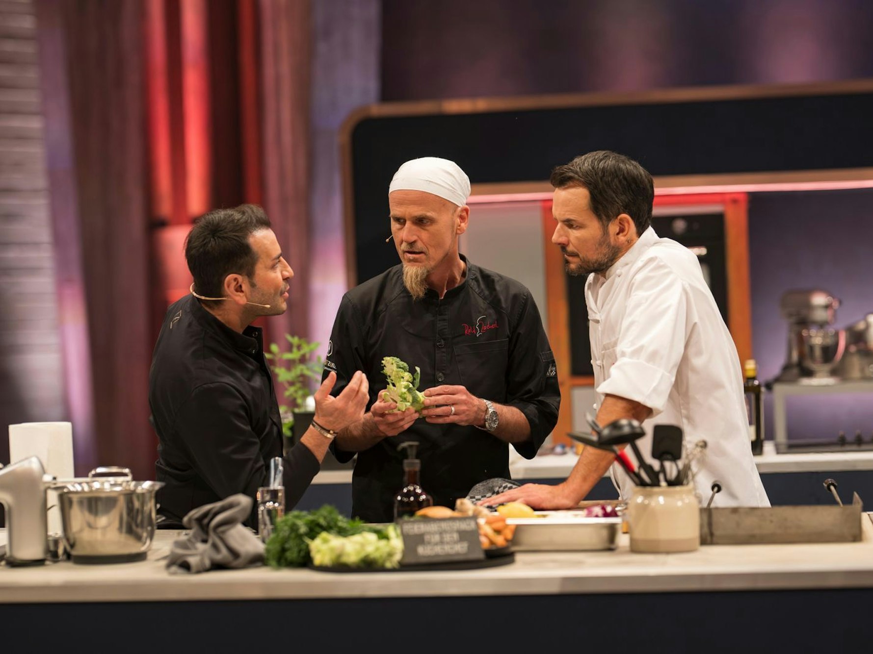 Drei Männer stehen an einem Tisch, auf dem Lebensmittel liegen.