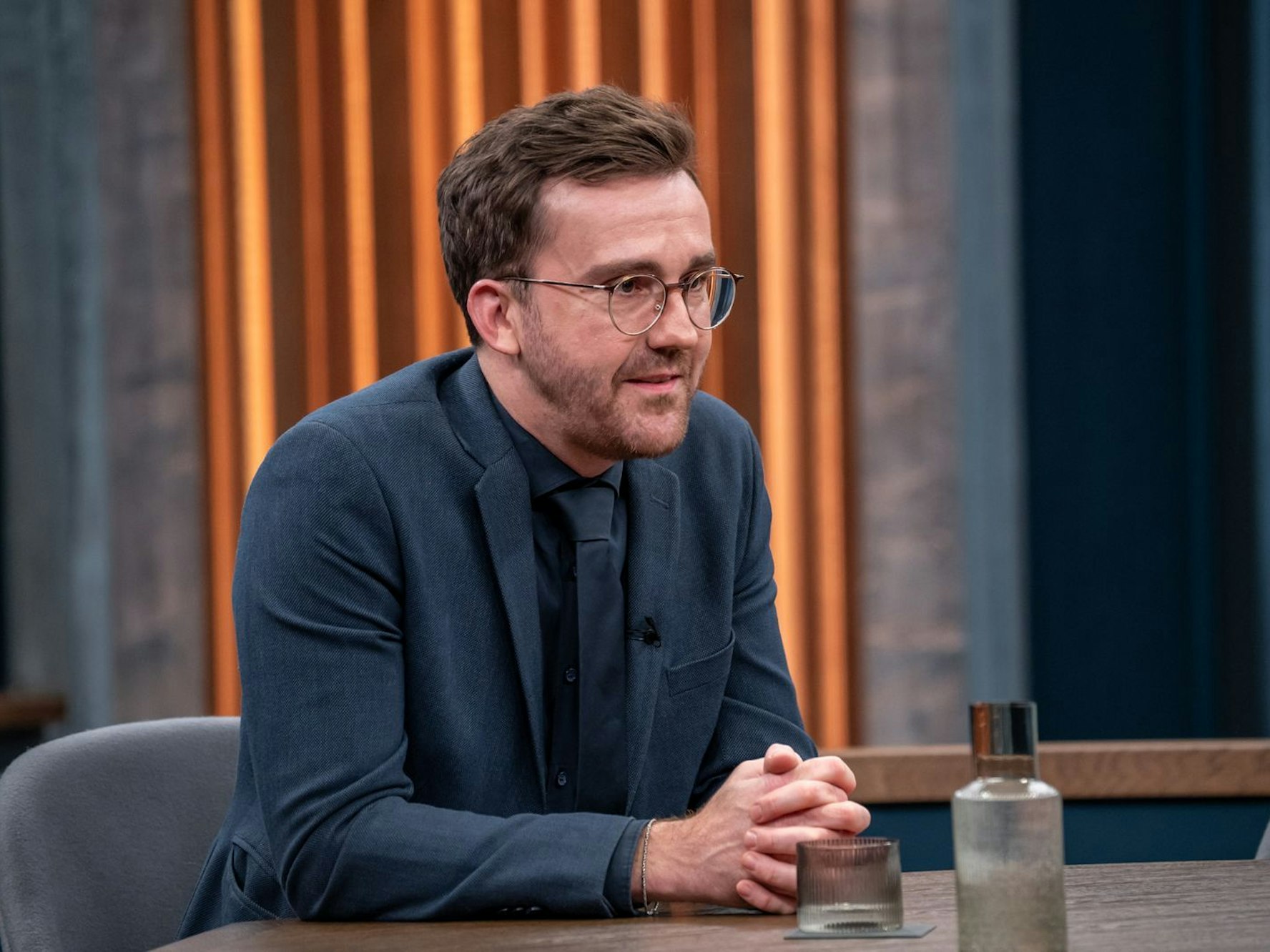 Ein Mann sitzt mit gefalteten Händen an einem Tisch.