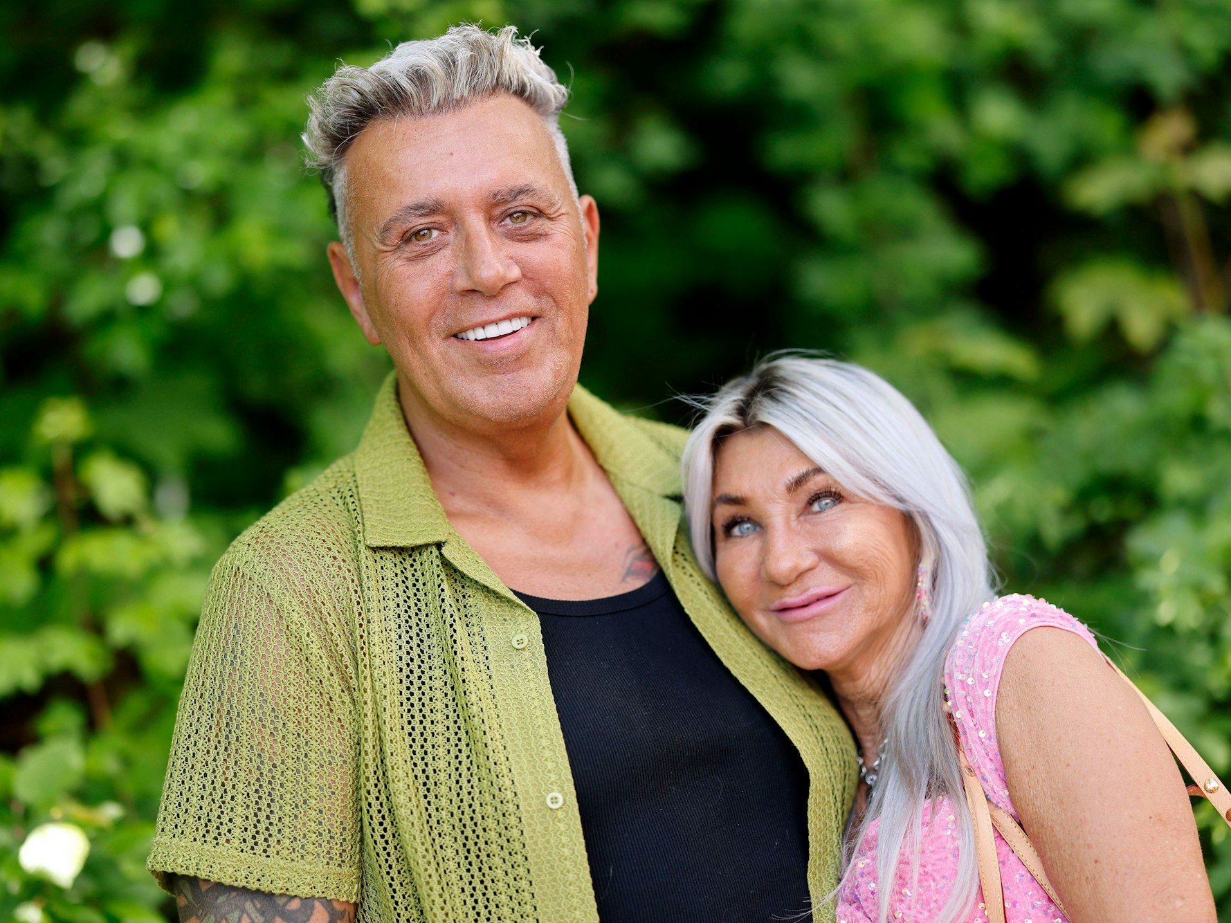 Ein Mann und eine Frau lächeln warmherzig vor einem natürlichen grünen Hintergrund