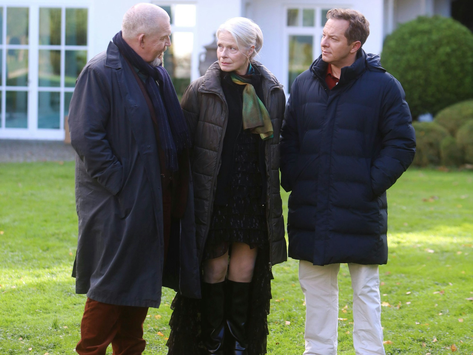 Tatort-Dreharbeiten im Hahnwald. Dietmar Bär, Corinna Kirchhoff und Trystan Pütter stehen im Garten einer Villa.