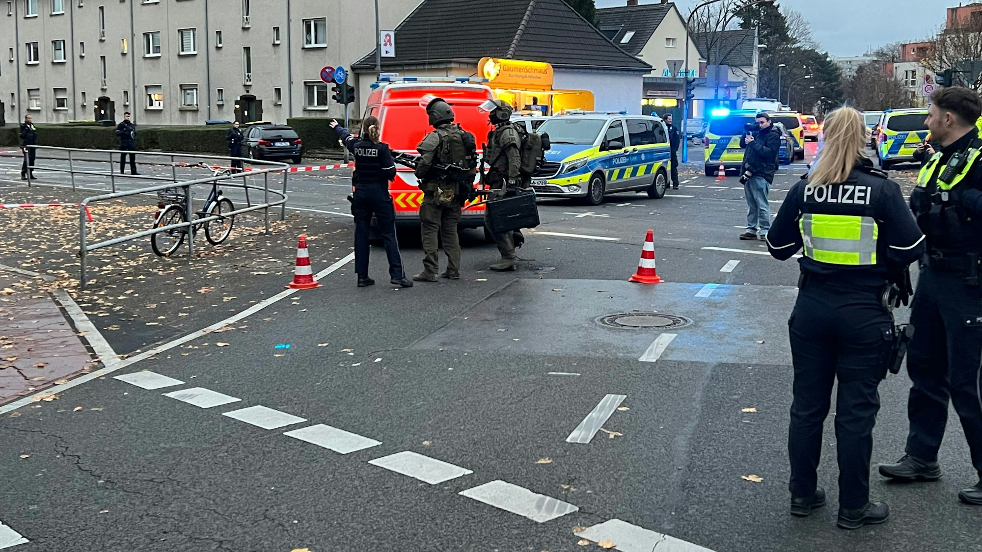 Polizeikräfte, teilweise vermummt und schwer bewaffnet, stehen auf einer Straße, die abgesperrt ist.