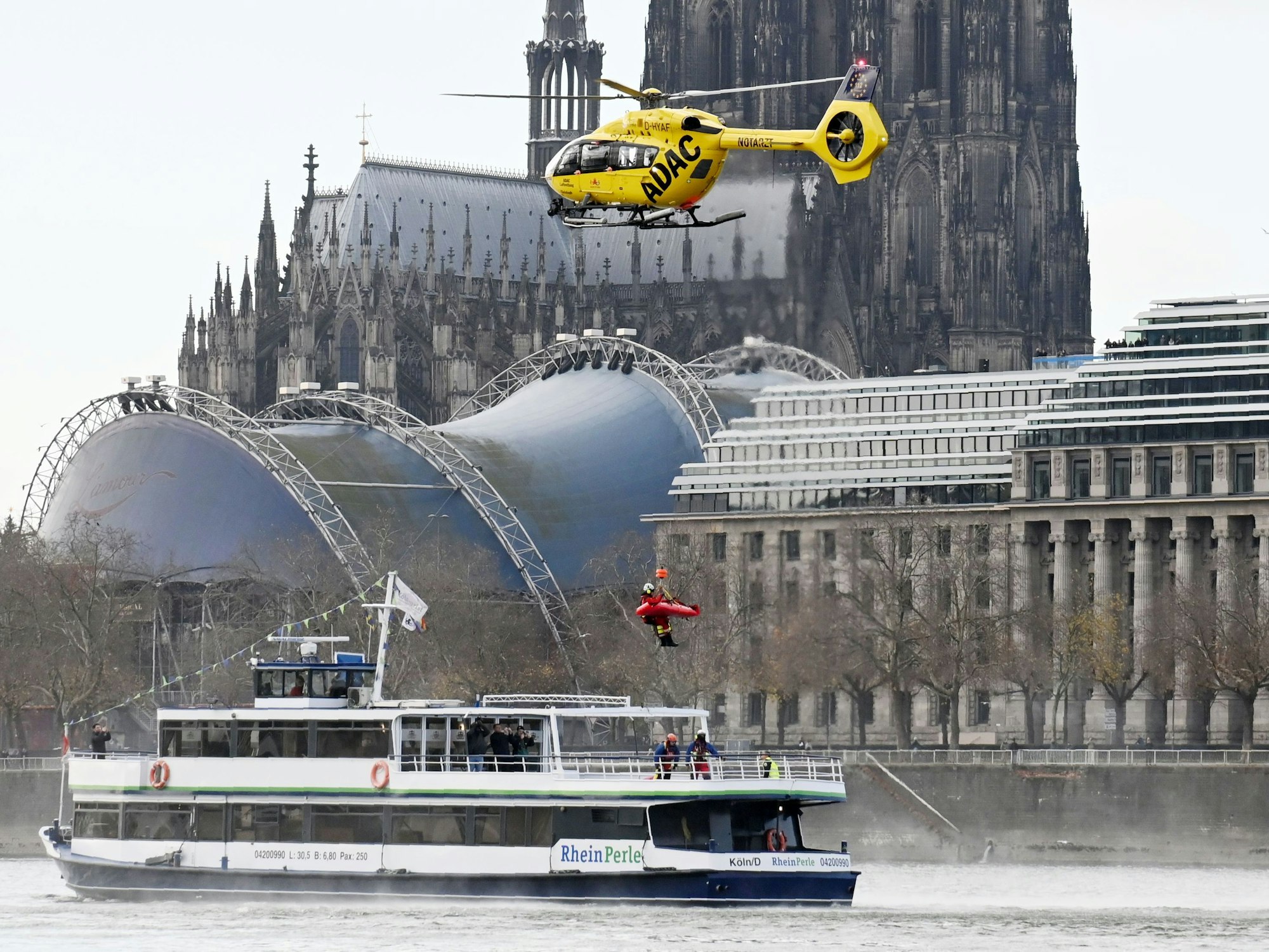 Eine Person hängt an einem Seil an einem Hubschrauber, unter ihr ein Schiff mit dem Namen Rheinperle.