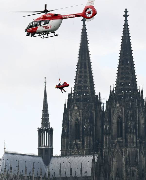 Eine Person hängt an einem Seil an einem Hubschrauber und schwebt an den Spitzen des Kölner Doms vorbei.