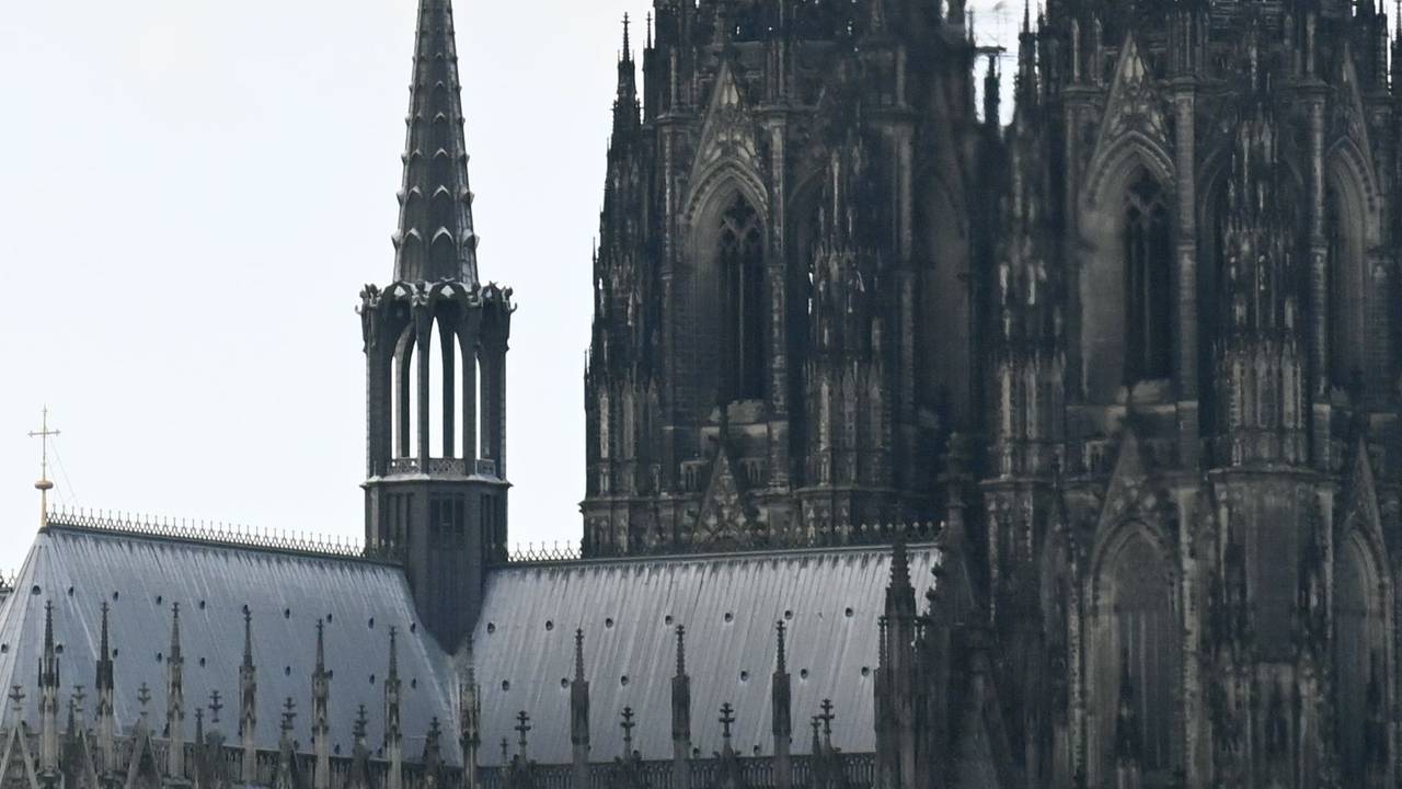 Eine Person hängt an einem Seil an einem Hubschrauber und schwebt an den Spitzen des Kölner Doms vorbei.