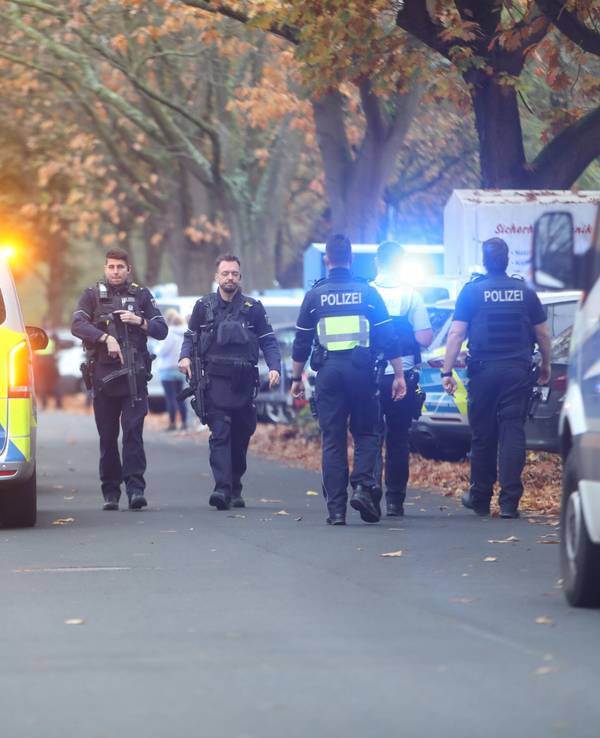 Einsatzkräfte laufen über eine Straße an einem Polizeifahrzeug vorbei.