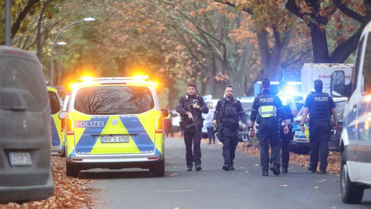 Einsatzkräfte laufen über eine Straße an einem Polizeifahrzeug vorbei.