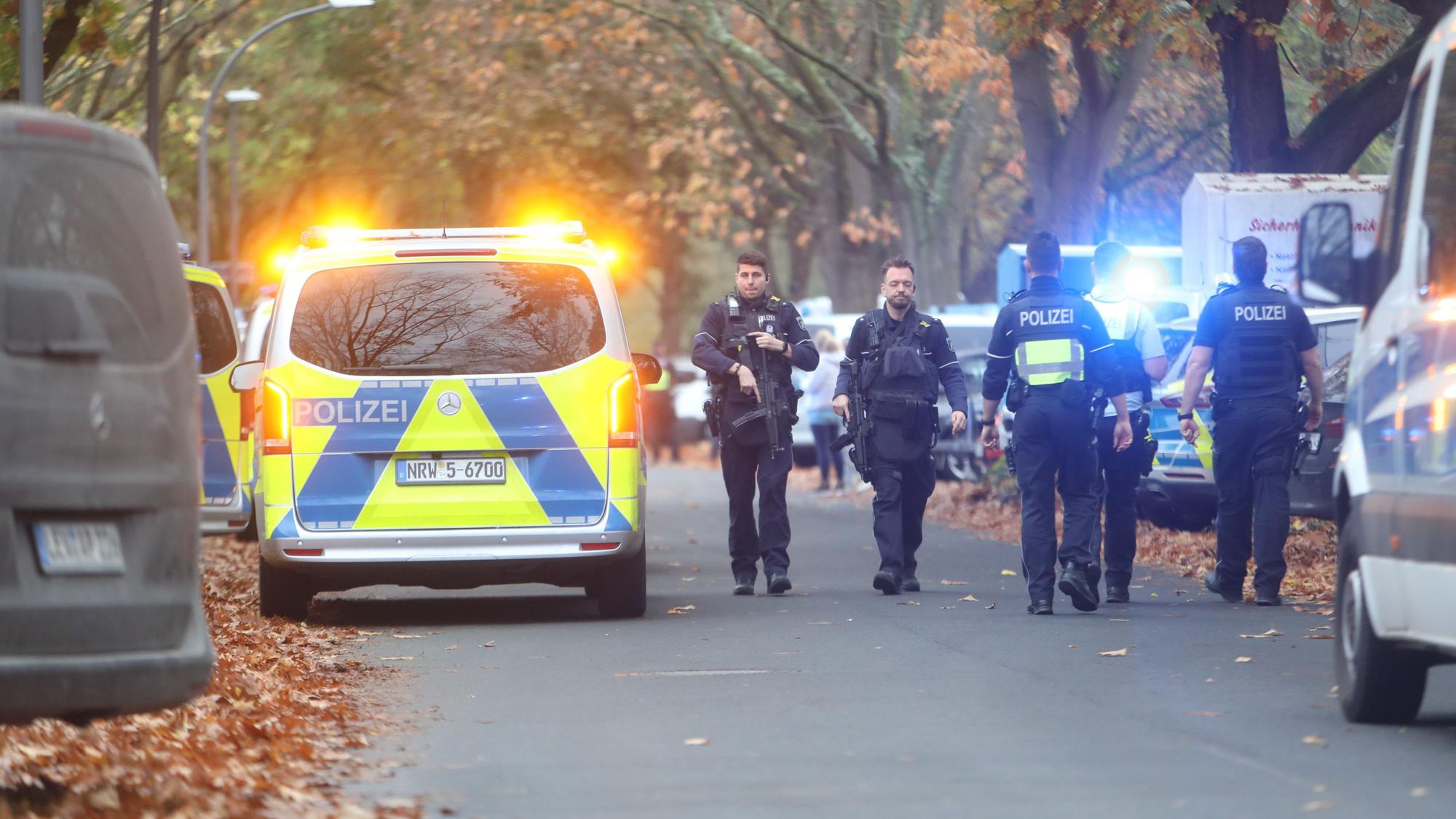 Einsatzkräfte laufen über eine Straße an einem Polizeifahrzeug vorbei.