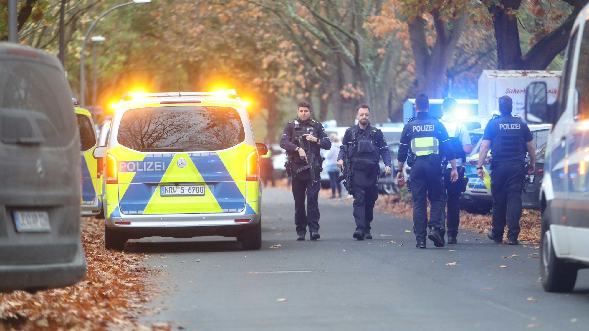 Einsatzkräfte laufen über eine Straße an einem Polizeifahrzeug vorbei.