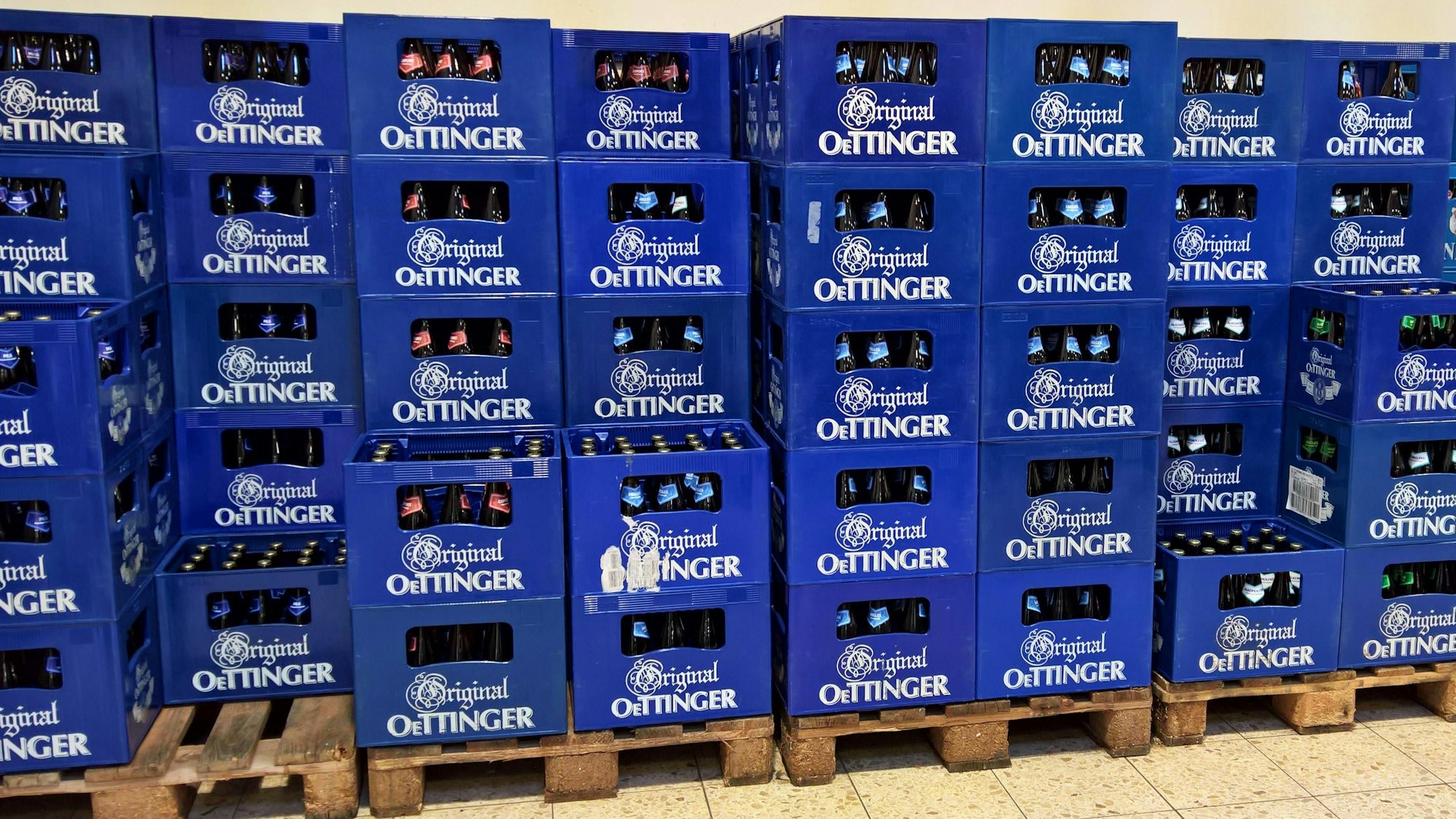 Gestapelte blaue Bierkästen der Oettinger Brauerei mit Flaschen auf Holzpaletten auf dem Boden