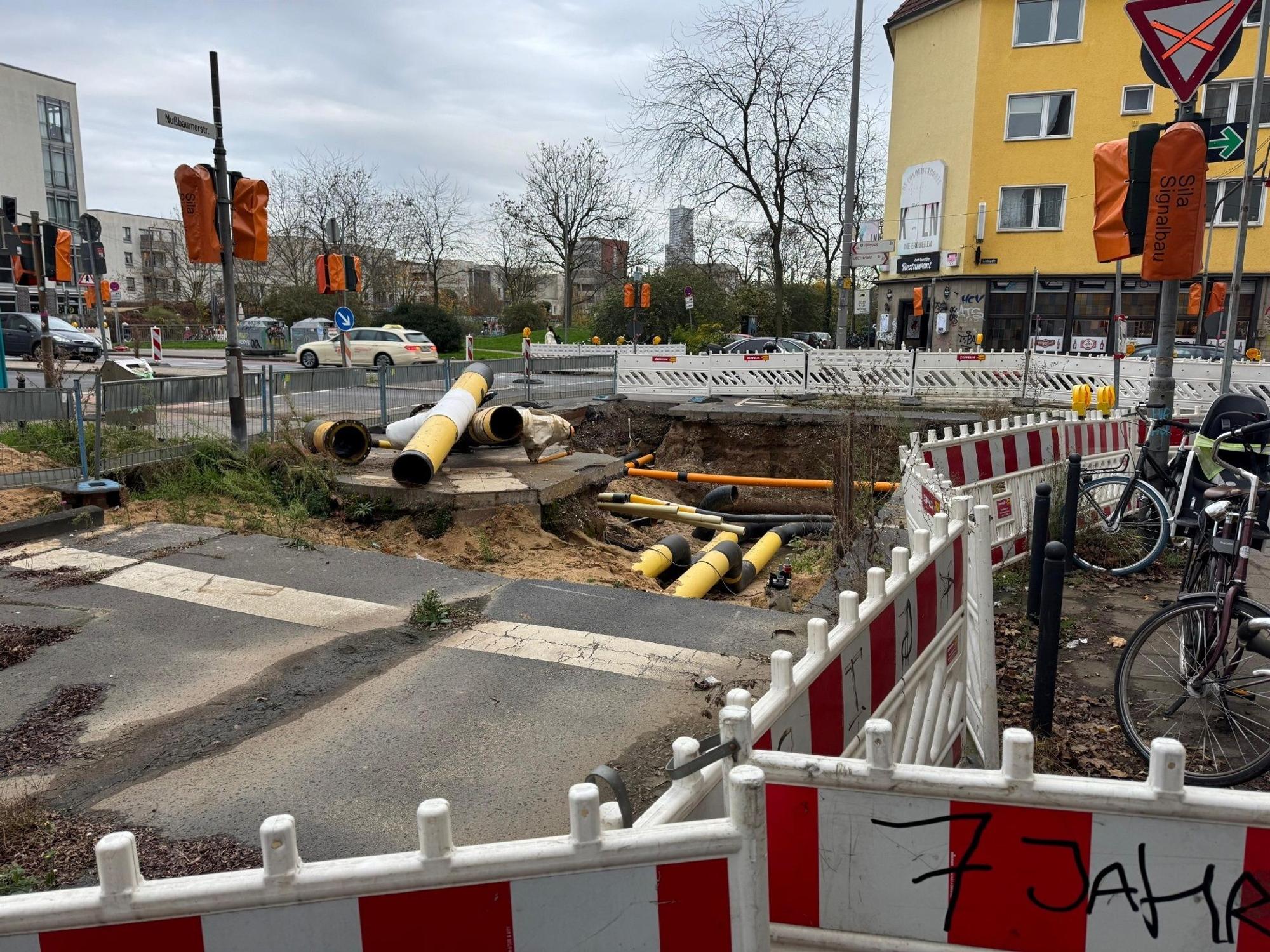 Längliche Baumaterialien liegen neben einem Loch, das im Asphalt einer Straße klafft.