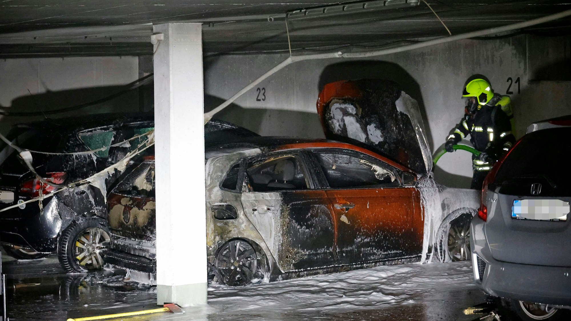 Feuerwehrmann löscht mit Schaum mehrere durch Brand beschädigte Autos in einer Tiefgarage