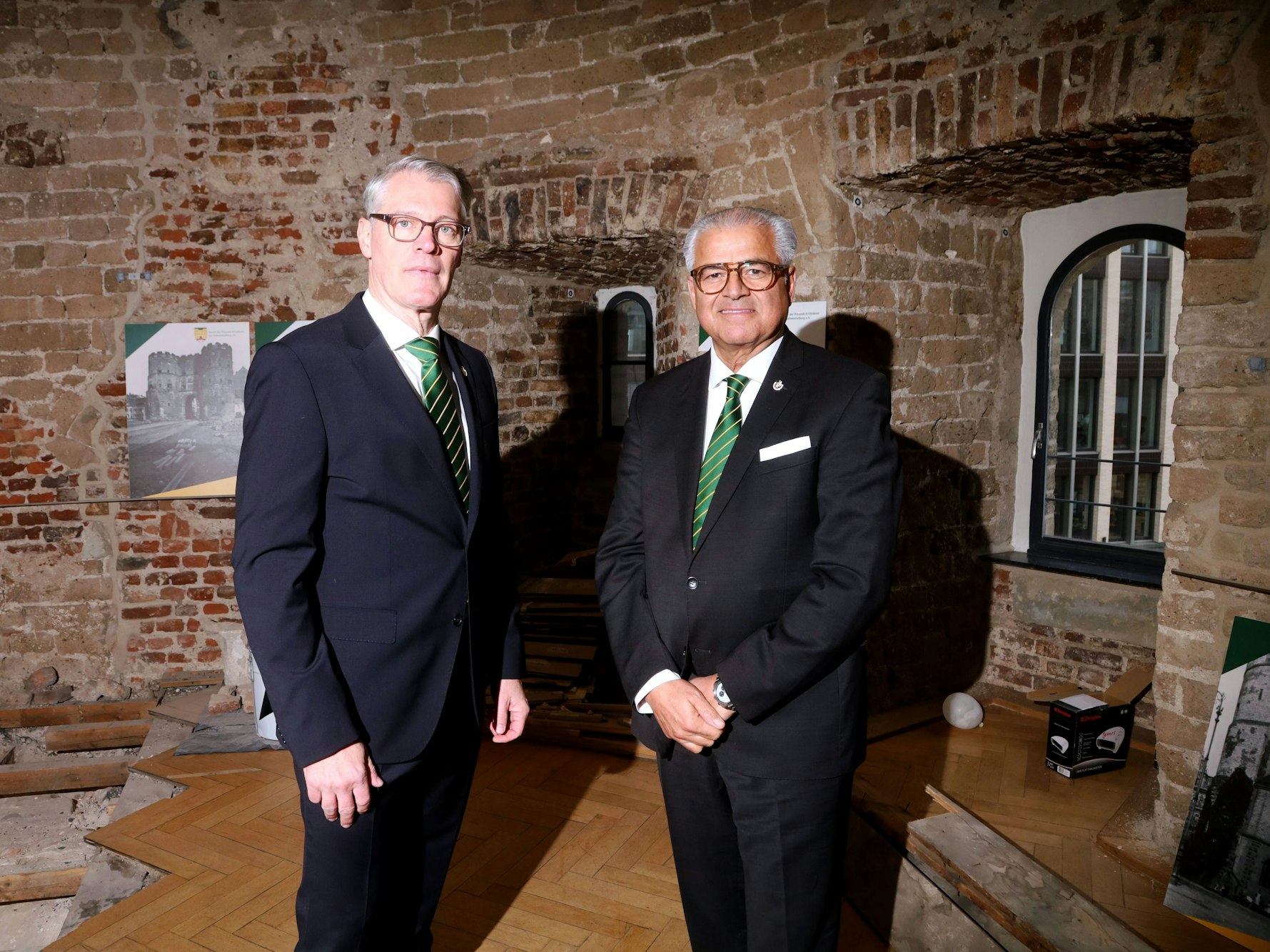 Zwei Männer, die den gleichen Anzug und die gleiche Krawatte tragen, stehen in einem alten Gemäuer.