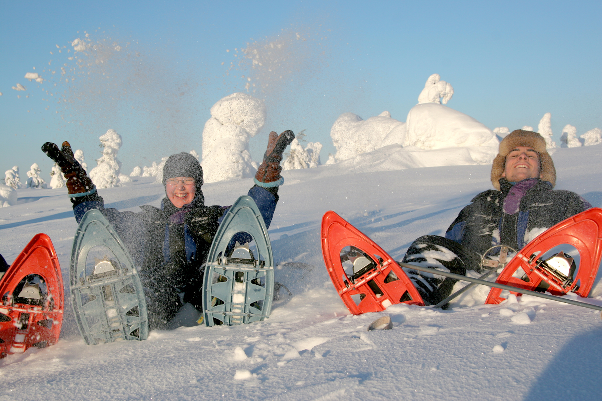 Das Bild zeigt zwei Personen, die während einer Schneeschuhwanderung im Schnee liegen und Spaß haben.