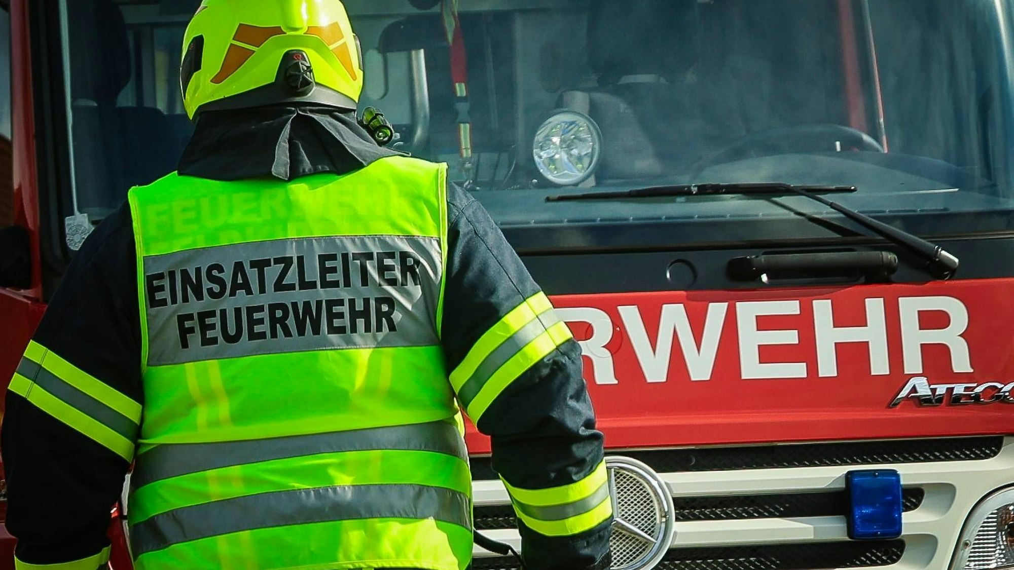 Ein Einsatzleiter der Feuerwehr mit Helm und Warnweste vor einem roten Feuerwehrauto