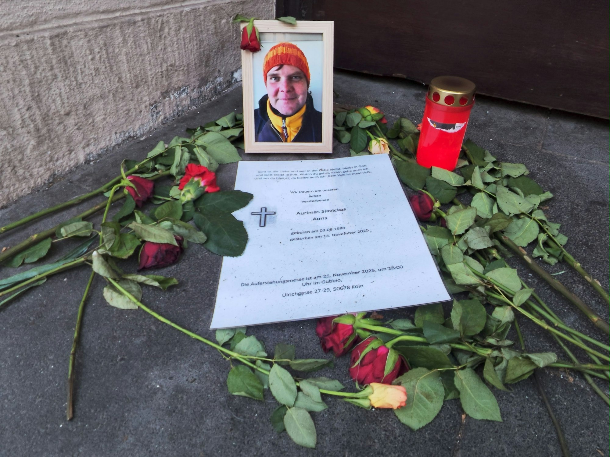 Vor einem Foto eines Mannes liegen Rosen und ein Zettel, daneben steht eine Kerze.