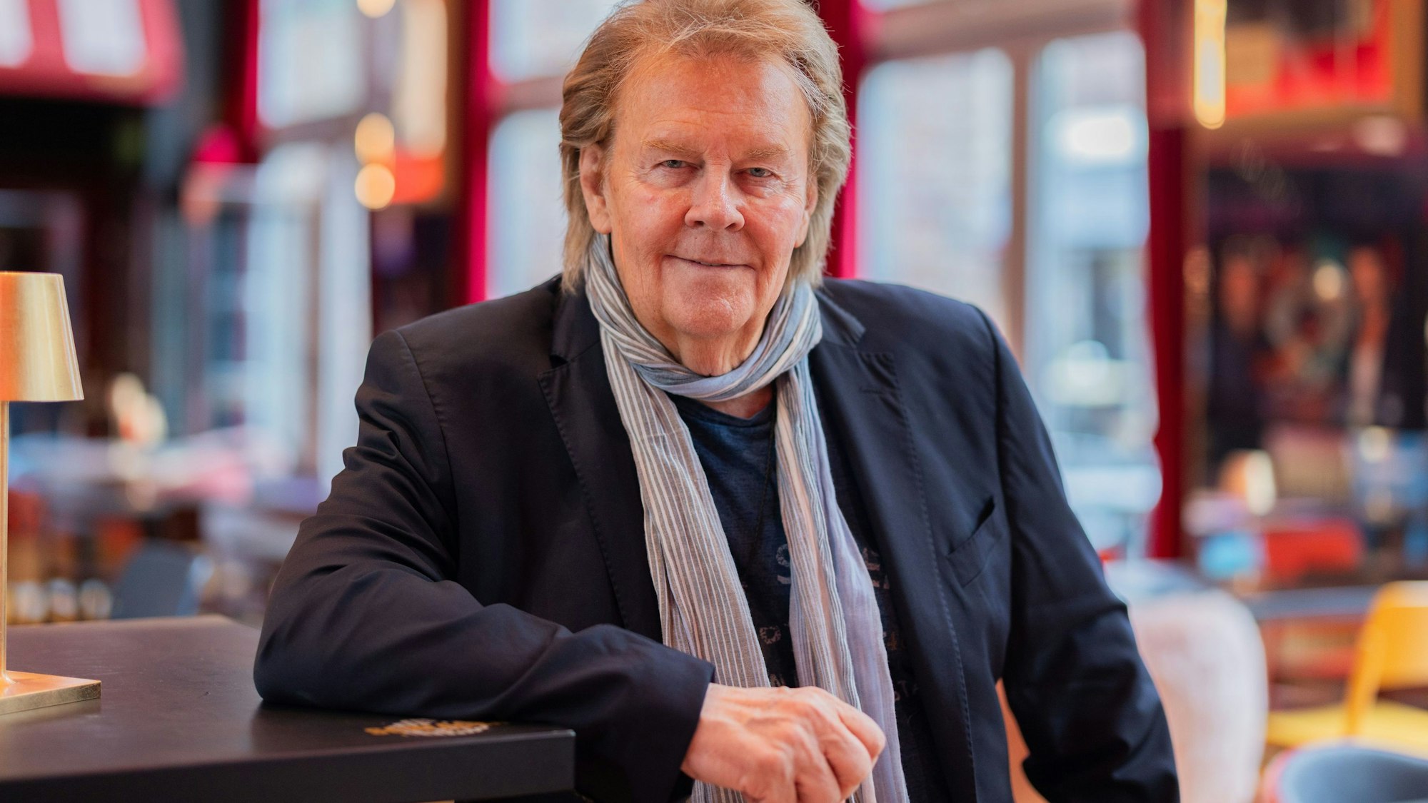 Ein Mann steht in einem Café und stützt einen Arm auf einen Holztresen.