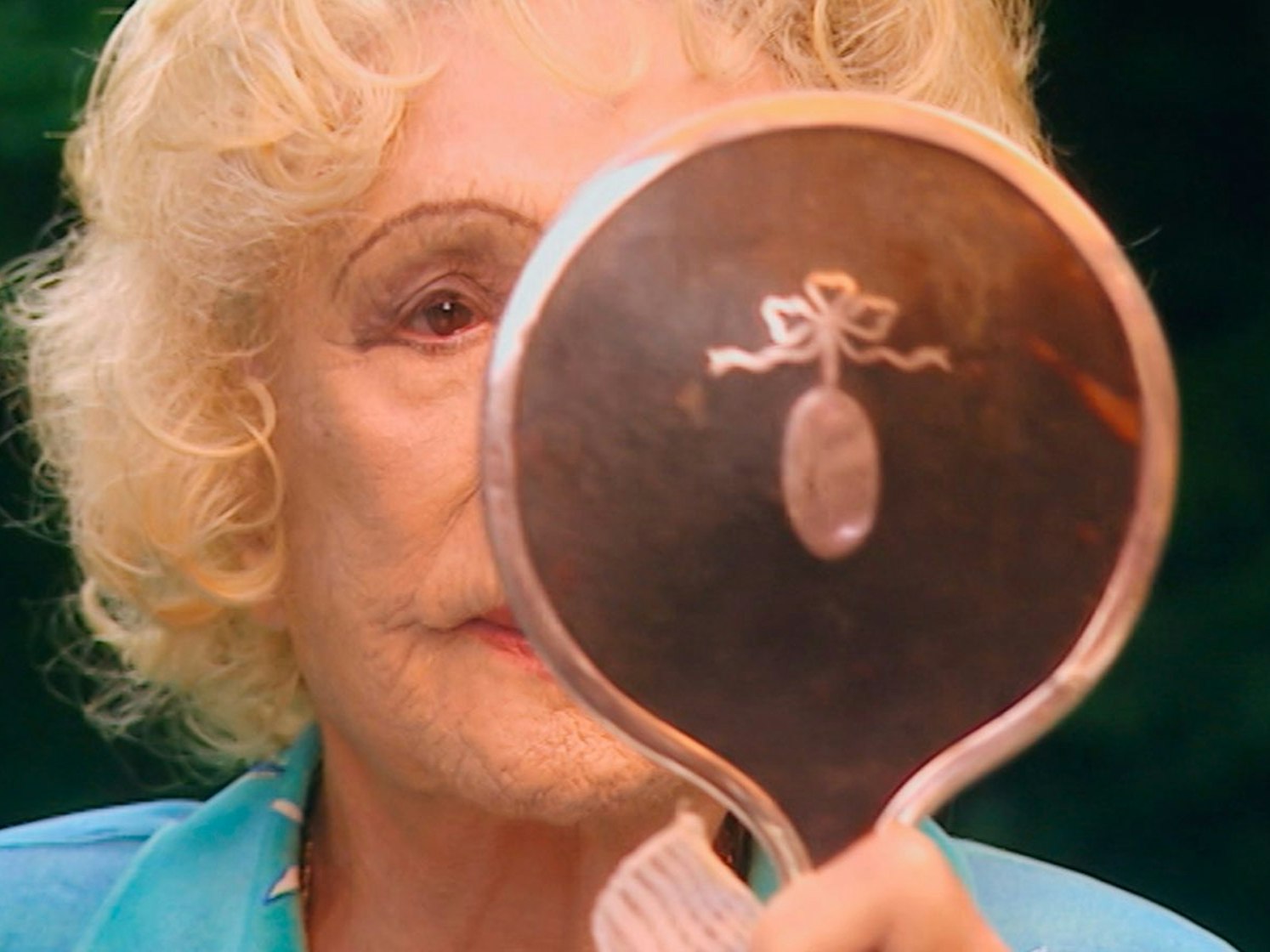 Eine ältere Frau guckt sich in einem Handspiegel an.