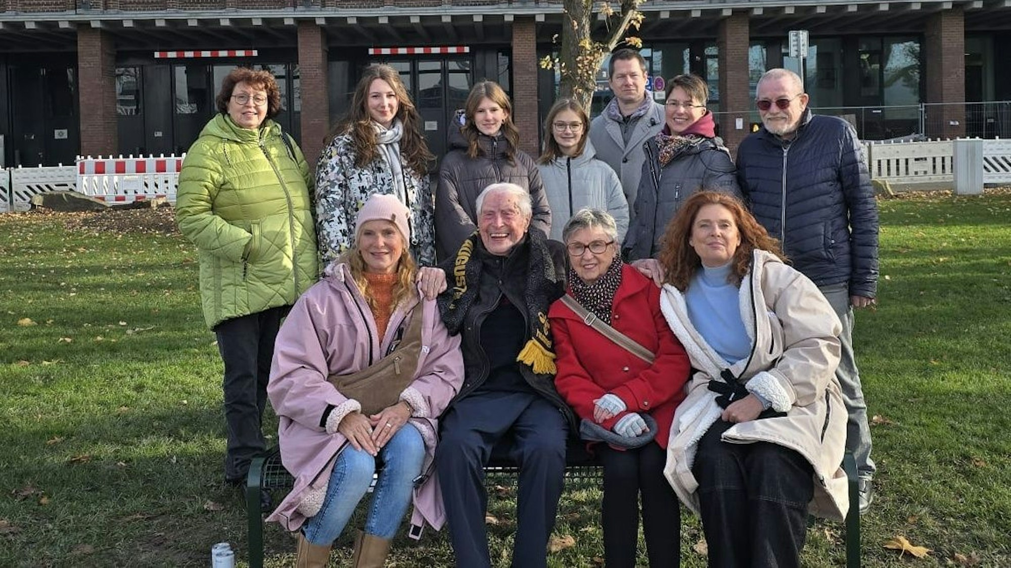 Ludwig Sebus sitzt umrahmt von seiner Familie auf seiner Bank am Rheinufer.