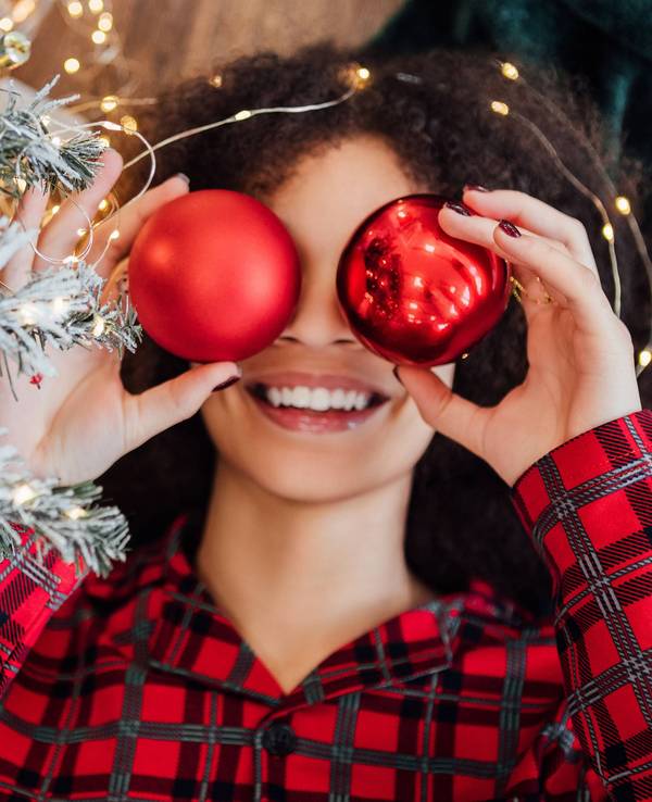Eine Frau hält sich rote Weihnachtskugeln vor die Augen.