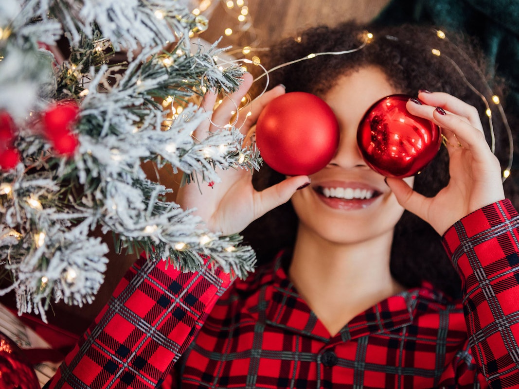 Eine Frau hält sich rote Weihnachtskugeln vor die Augen.
