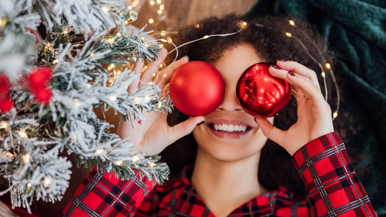 Eine Frau hält sich rote Weihnachtskugeln vor die Augen.