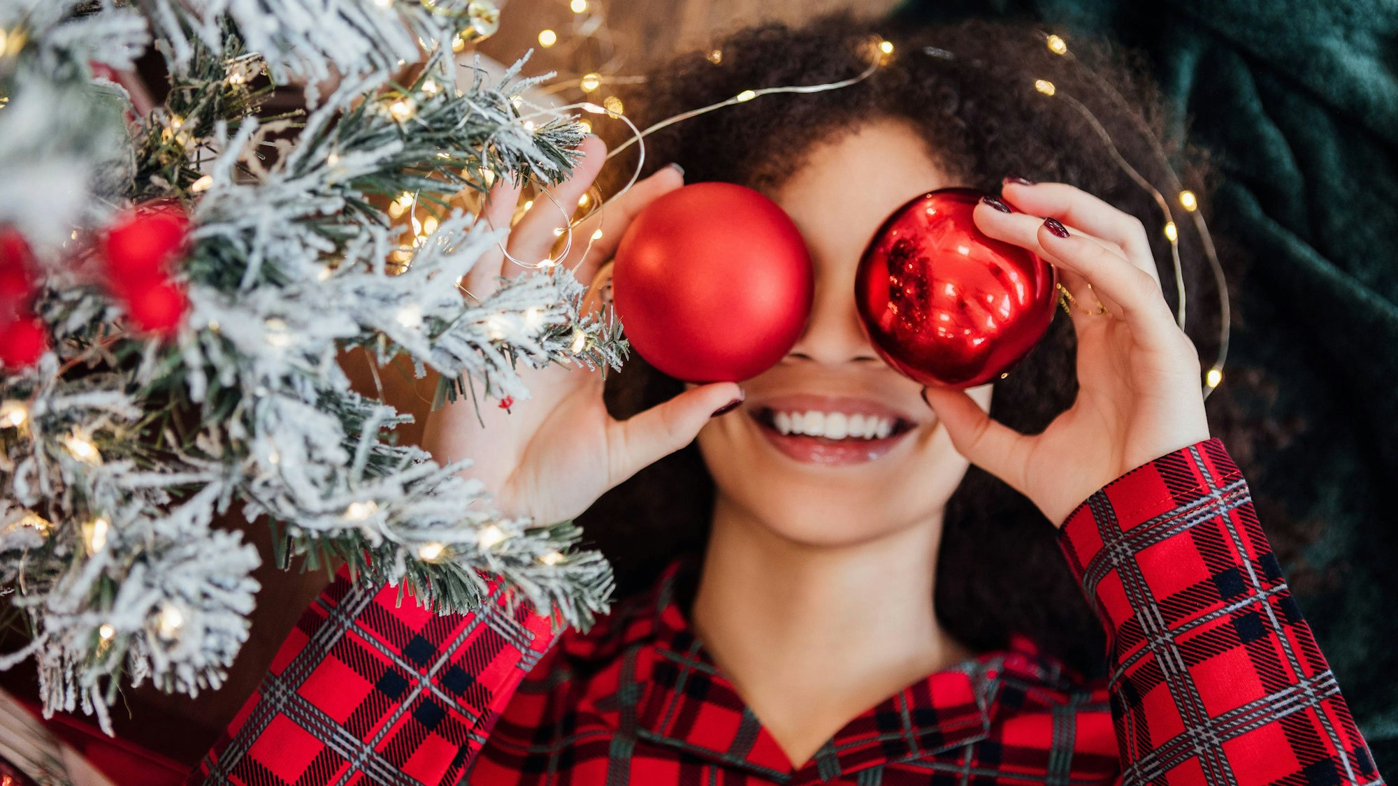 Eine Frau hält sich rote Weihnachtskugeln vor die Augen.