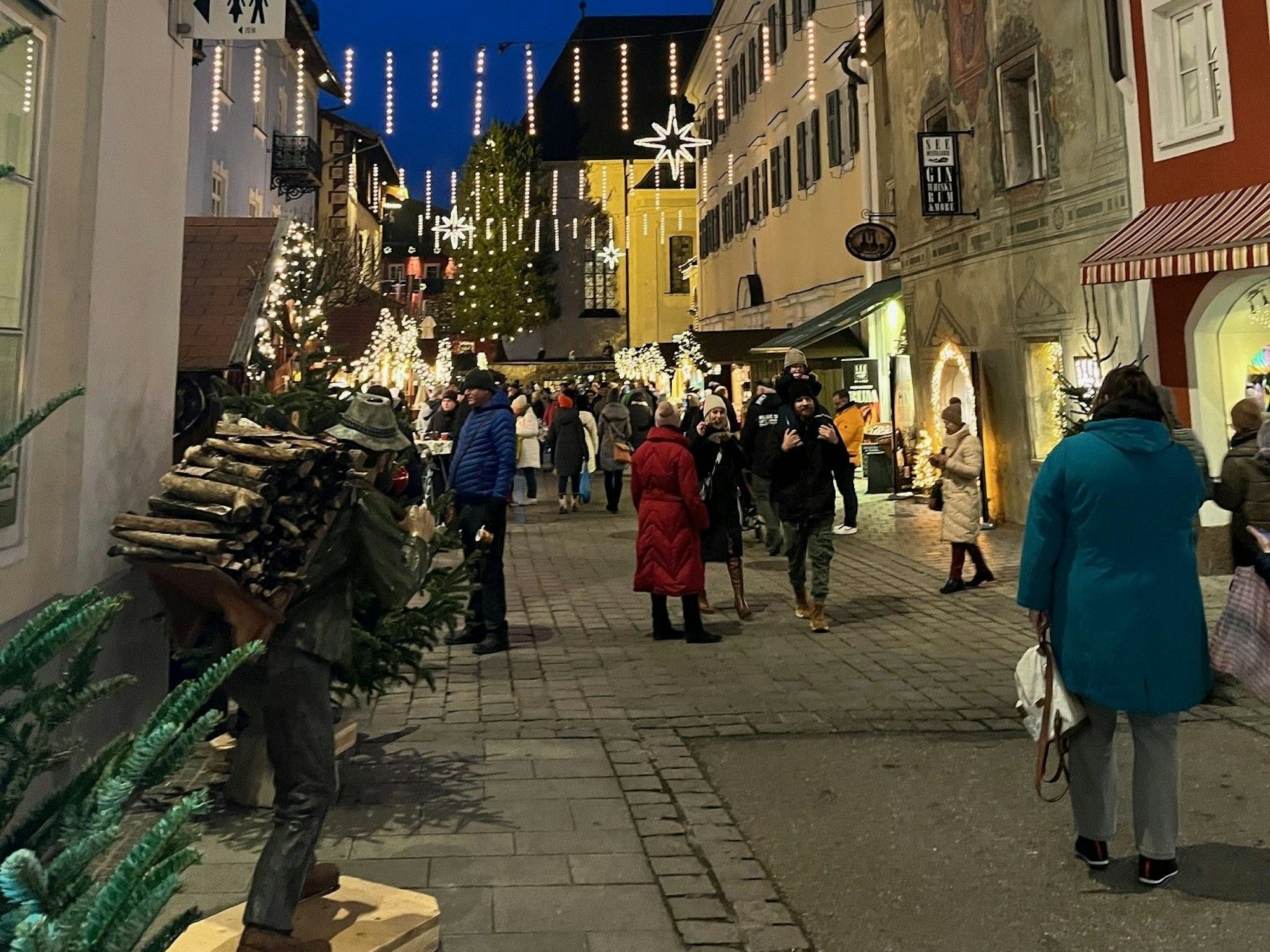 Menschen gehen durch eine adventlich geschmückte und beleuchtete Gasse.