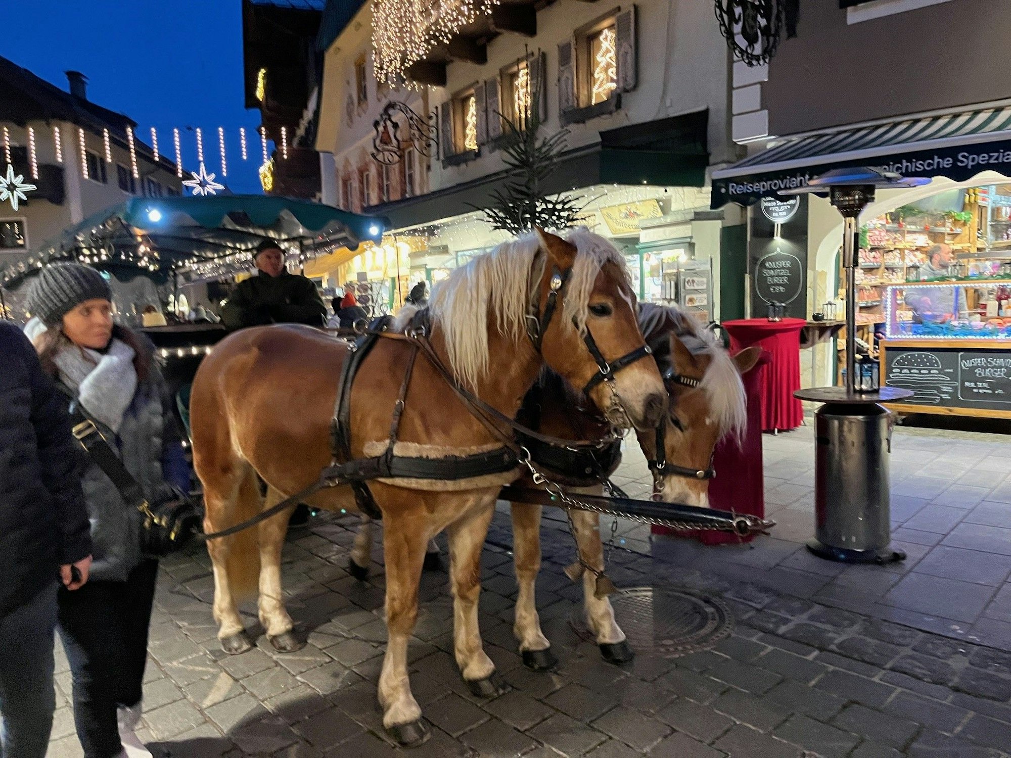 Eine Pferdekutsche mit zwei Haflingern steht in einer weihnachtlich geschmückten Einkaufsstraße.