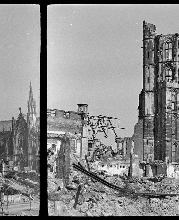 Eine halb zerbombte Kirche ragt auf einem Schwarzweiß-Foto in die Höhe, im Hintergrund der Kölner Dom.