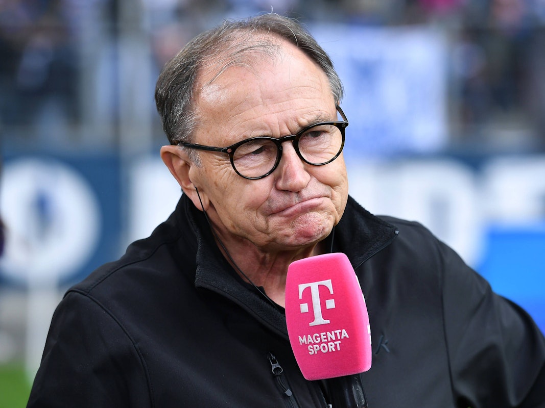 Ewald Lienen mit einem Mikrofon von MagentaSport.