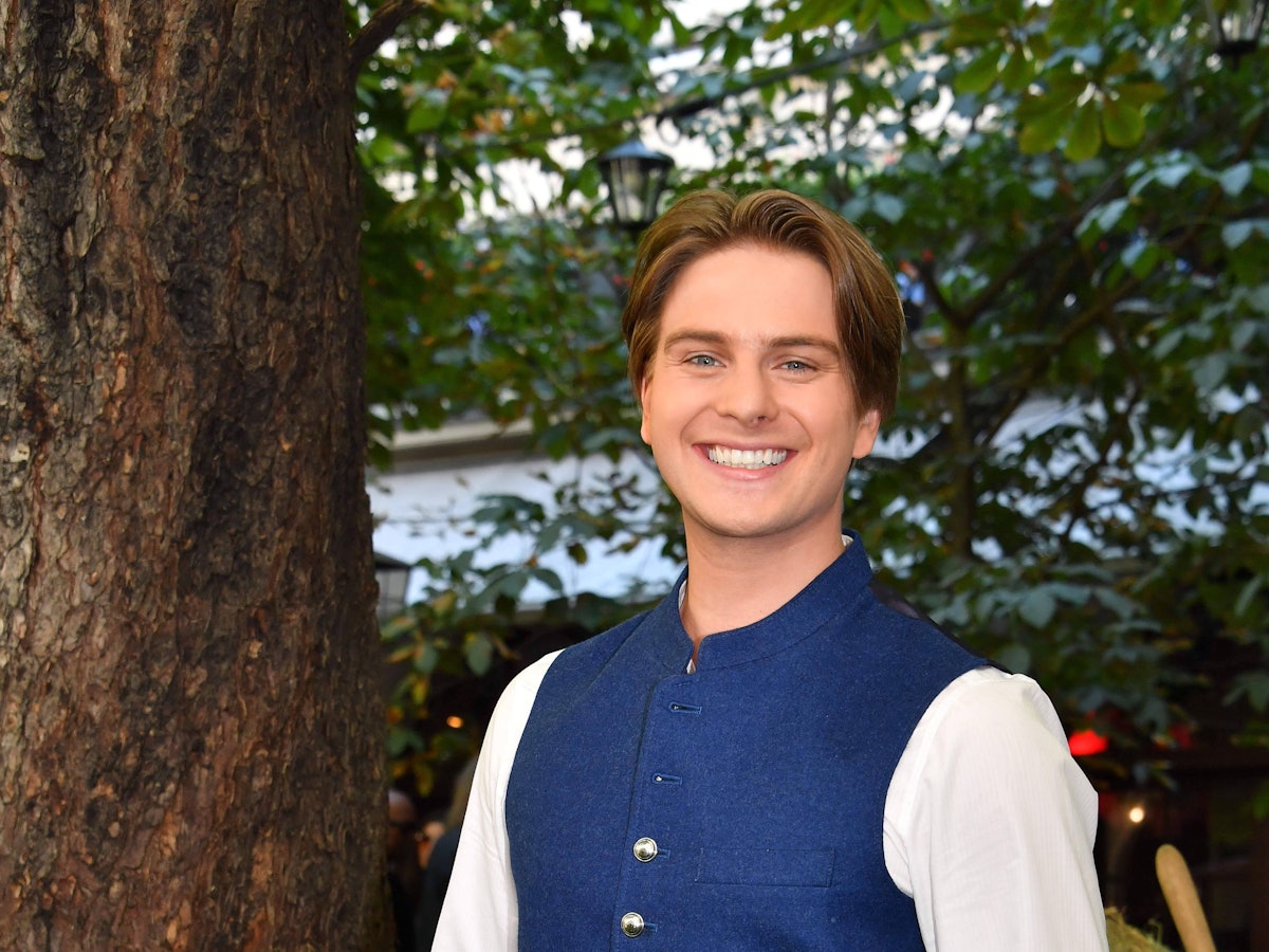 Ein junger Mann in weißem Hemd mit blauer Trachtenweste lacht freundlich in die Kamera.