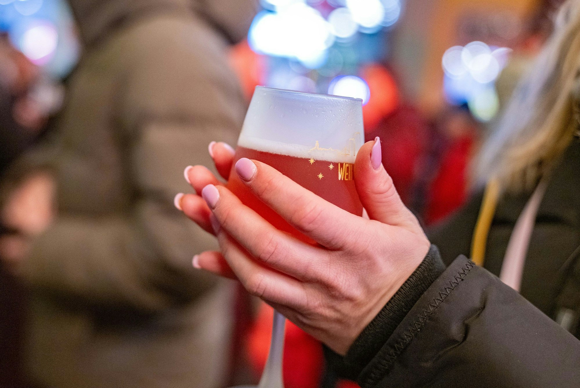 Eine junge Frau wärmt sich die Hände an einem Rosé-Glühwein.