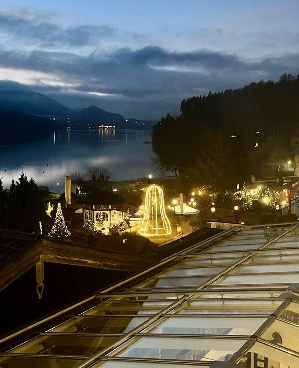 Dämmerung mit einem weihnachtlich geschmückten Haus mit tausenden Lichtern auf einen See und einen Bergrücken im Hintergrund.
