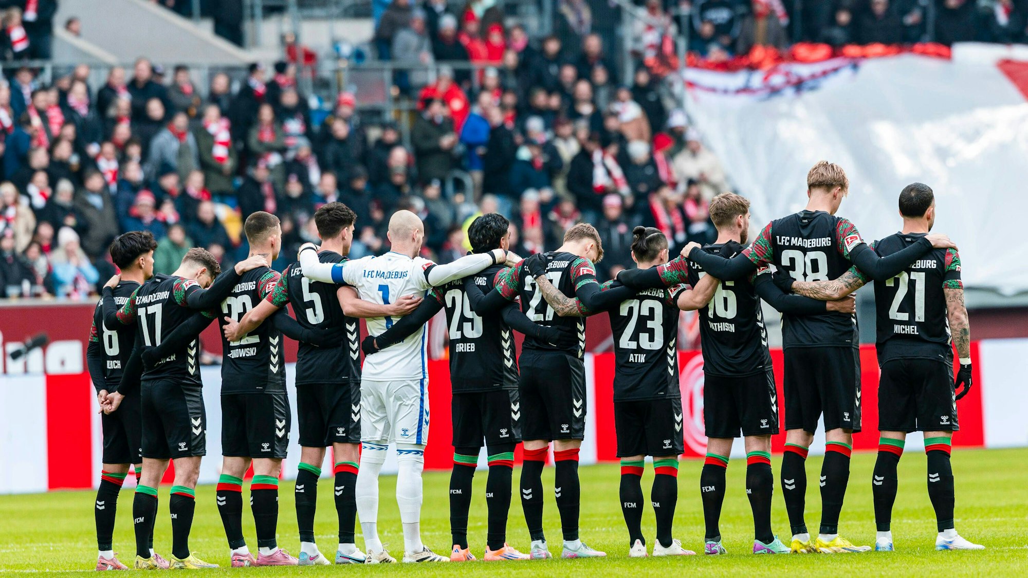 Spieler des 1. FC Magdeburg stehen Arm in Arm vor dem Anpfiff zusammen. Die Partie gegen Fortuna Düsseldorf wurde von einem medizinischen Notfall überschattet.
