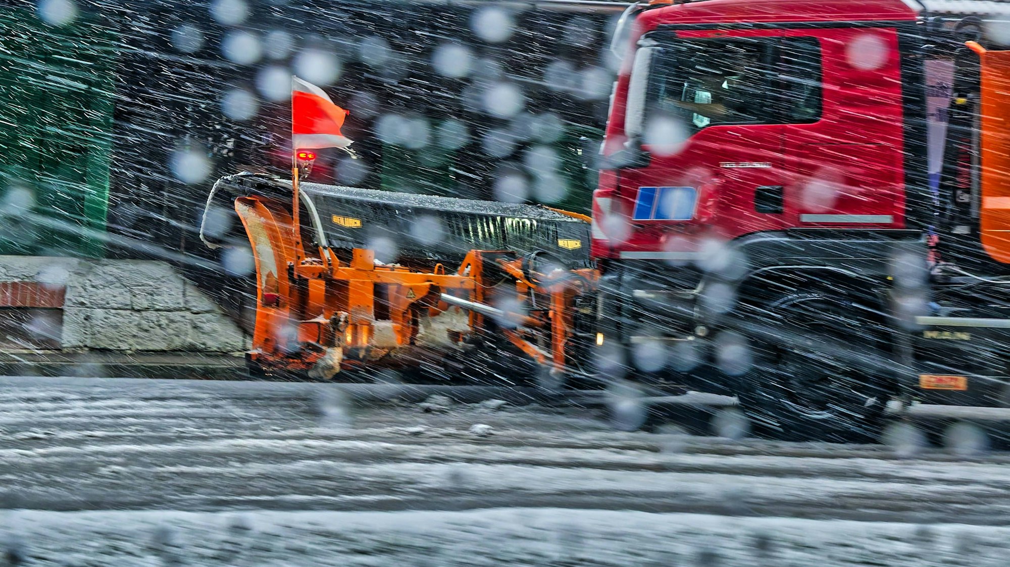 Ein roter Schneepflug-Lastwagen fährt bei starkem Schneefall auf einer winterlichen Straße in Deutschland
