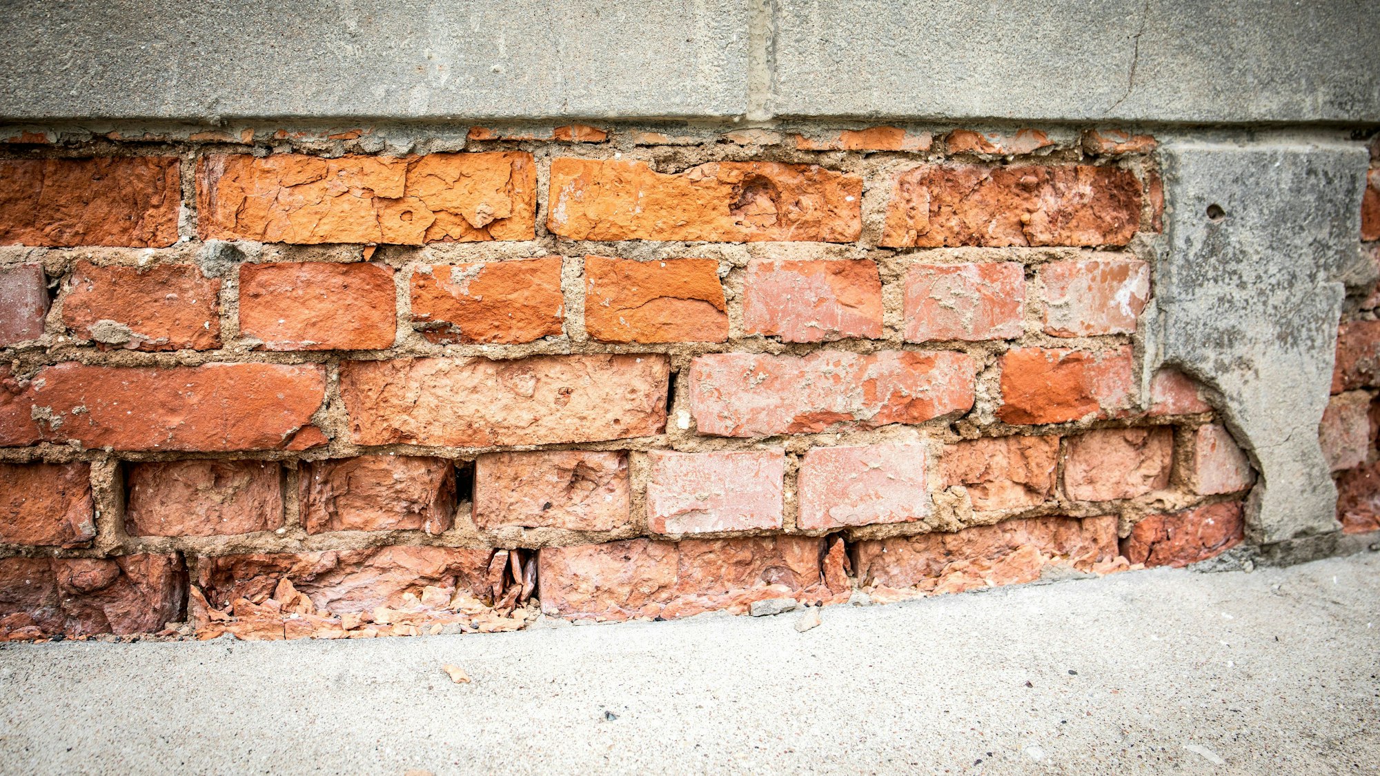 Nahe Einstellung einer verwitterten Ziegelmauer unter einer grauen Betonleiste und körnigem Boden