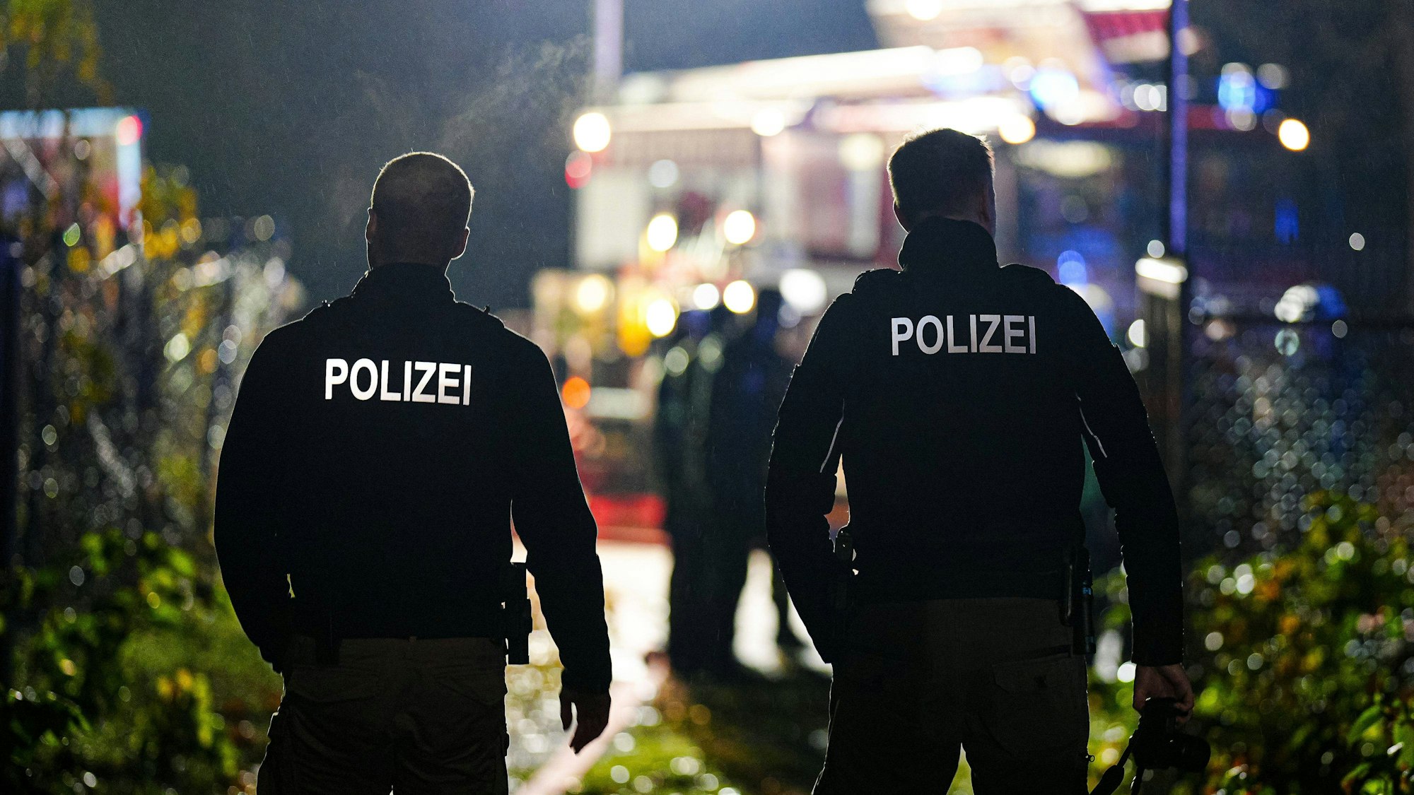 Zwei Polizisten von hinten bei Nacht, im Hintergrund verschwommenes Blaulicht